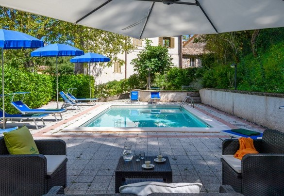 Pool area with sun loungers and umbrellas, enclosed by green hedges - Acquanera