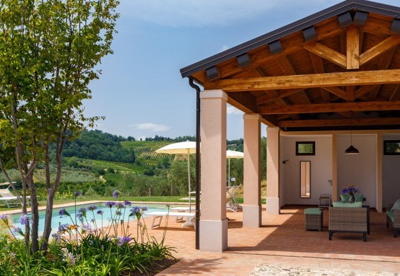 Large paved pergola furnished with a seating area overlooking the swimming pool and the valley below – Ca’ Pellicciano