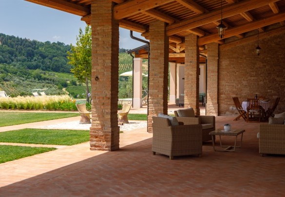 Large paved pergola furnished with a dining table and a seating area overlooking the swimming pool and the valley below – Ca’ Pellicciano