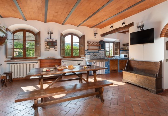 L’ambiente open space in cui si trova un salone con tavolo e con camino e la cucina in muratura al piano terra – Casa Paggetti