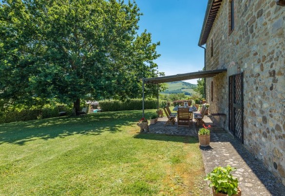 La pergola sul retro vicino alla cucina è attrezzata con tavolo da pranzo, più distante verso la siepe che delimita il confine si trova il barbecue in muratura- Casale del Viaggiatore