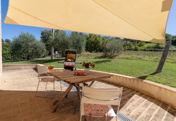 Zona ombreggiata, arredata con tavolo, sedie e barbecue - Casale La Cascina  