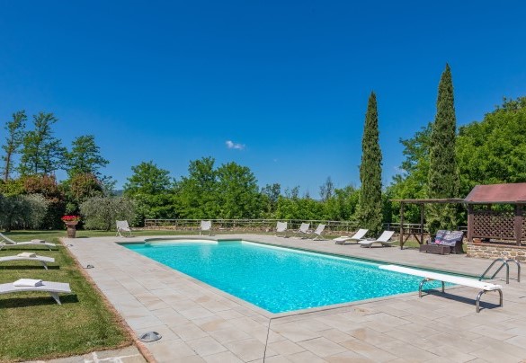Il bordo piscina lastricato in pietra e circondato da superfici a prato - Casale La Splendida