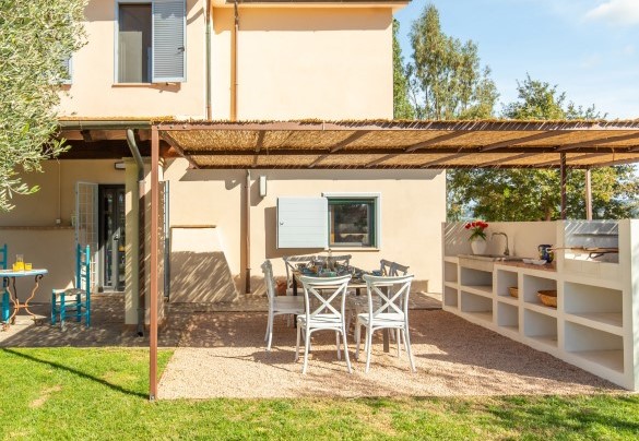 La pergola con tavolo da pranzo e cucina in muratura accessoriata con barbecue a carbonella, piastre a induzione, lavabo e piani di lavoro - Casale Rondinella