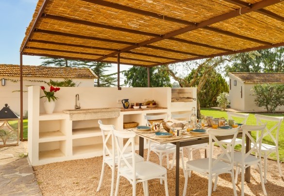 La pergola con tavolo da pranzo e cucina in muratura accessoriata con barbecue a carbonella, piastre a induzione, lavabo e piani di lavoro - Casale Rondinella
