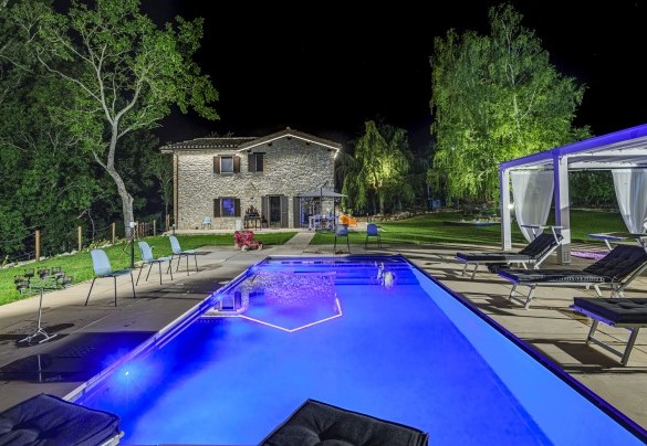 Piscina illuminata di notte con area lounge e lettini - Casalino Galassi