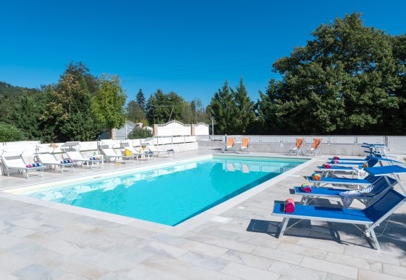 L’area solarium, pavimentata in gres porcellanato antiscivolo effetto pietra, è attrezzata con lettini, sdraio, tavolini e ombrelloni – Cascina Marianna