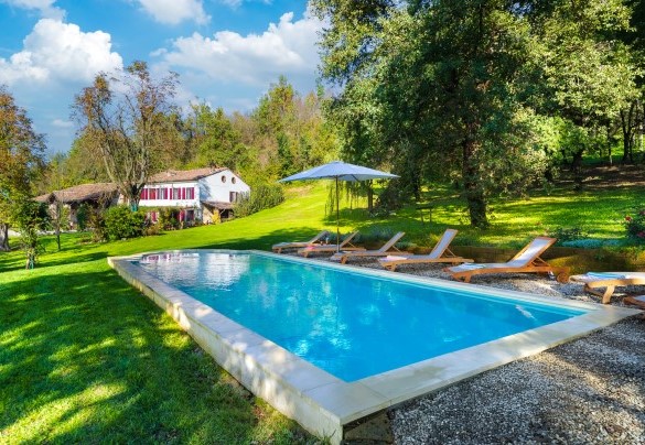 The intense blue color of the swimming pool goes well with the greenery of the garden and tall trees – Cascina Monferrato