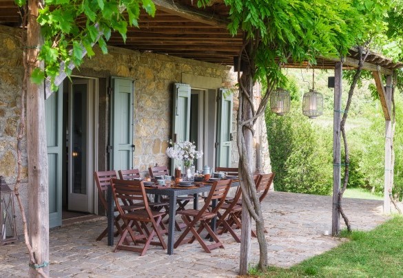 Il porticato, avvinto da rampicanti di vite, in comoda posizione all’uscita delle porte finestra della zona giorno, è arredato per pranzare all’aperto – Cinque Cipressi