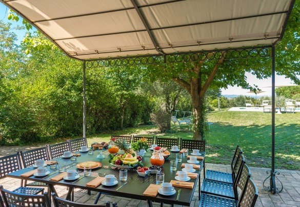 Pergolato arredato con tavolo e sedie proprio davanti alla porta finestra della cucina ed adiacente alla piscina - Finestra su Siena