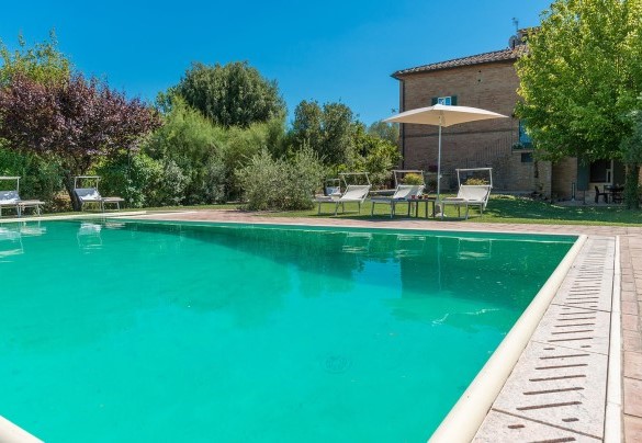 La piscina è bordata dalla zona prendisole con lettini e ombrelloni - Finestra su Siena