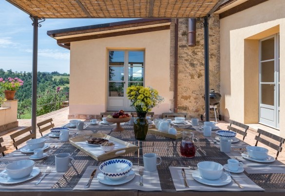 Un’ampia terrazza lastricata dove, protetti da un gazebo, sono posizionati tavolini, sedie, divani e un lungo tavolo per mangiare all’aperto – Il Colle di Donna Ilaria 