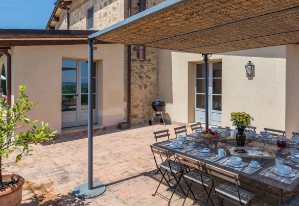 Un’ampia terrazza lastricata dove, protetti da un gazebo, sono posizionati tavolini, sedie, divani e un lungo tavolo per mangiare all’aperto – Il Colle di Donna Ilaria 