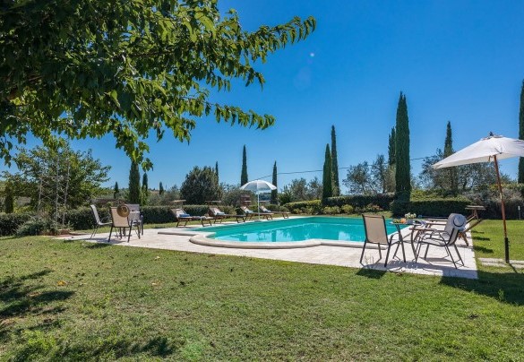 The pool area, in travertine paving and lawn, is completed by a shower, sunbeds, small tables and umbrellas – Il Fitto