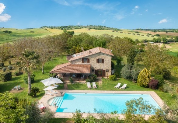 La piscina immersa nel verde del parco, con solarium attrezzato e il casale sullo sfondo – Il Noceto 