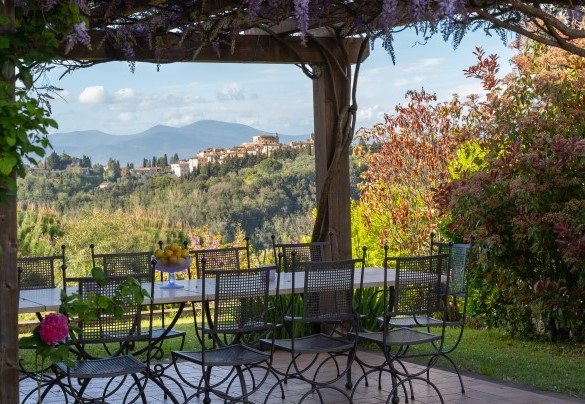 La zona pranzo all'aperto con tavolo in pietra e sedie allestita sotto il pergolato con un bel glicine – La villa nell’isola verde