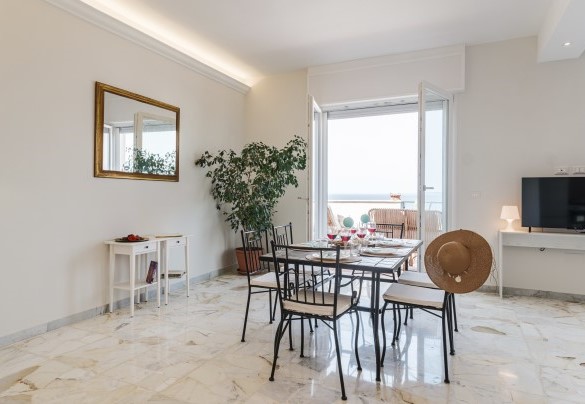 Dall'ingresso di questo attico situato al quinto piano, si accede in un luminoso e largo open space con finestre vista mare che accoglie la cucina e l’area pranzo. Nova Domus
