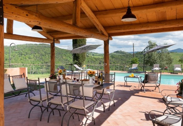La zona pranzo esterna, posta sotto una struttura in legno con illuminazione a pochi passi dal casale, dove sono presenti tavolo e sedie e un comodo salottino – Podere Capanne