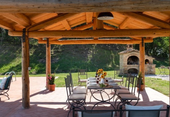 La zona pranzo esterna, posta sotto una struttura in legno con illuminazione a pochi passi dal casale, dove sono presenti tavolo e sedie e un comodo salottino – Podere Capanne