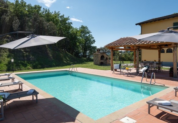 Intorno alla piscina troviamo la zona solarium con pavimentazione in cotto e il resto a prato, arredata con lettini prendisole e due ombrelloni – Podere Capanne