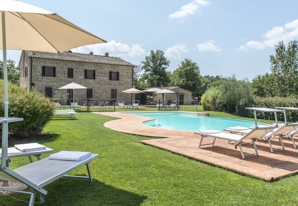 La zona solarium è pavimentata in cotto lungo il perimetro della vasca e poi delimitata da una spaziosa superficie a prato, su cui sono sistemati lettini, tavolini ed ombrelloni - Podere Sant’Eugenio
