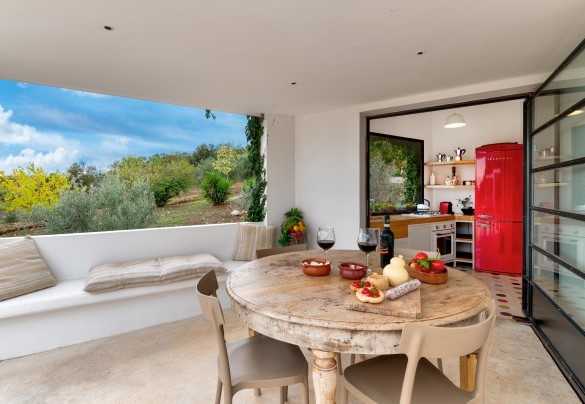Un’ampia porta finestra conduce dalla cucina della lamia principale alla sua zona pranzo esterna, ricavata sotto il portico in muratura – Trulli Santa Pazienza