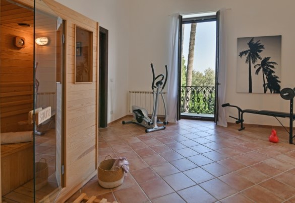 Una stanza luminosa ospita degli attrezzi da palestra ed una sauna finlandese - Villa Afrodite 