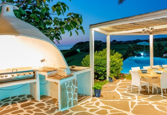 External living room with the large 12-seater granite table near the pool and the area with barbecue and outdoor professional kitchen – Villa Ambra