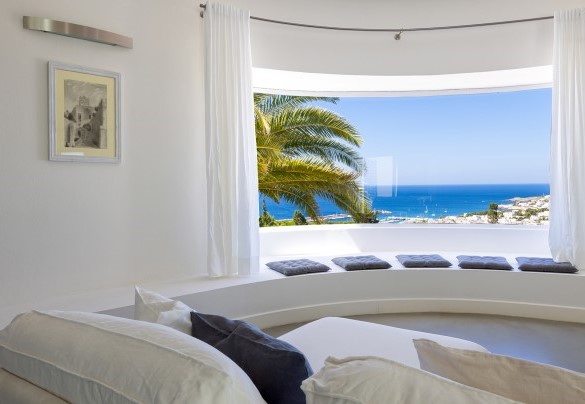 A large living area furnished with a spectacular dining table and sofas placed in front of large windows that frame the boundless panorama - Villa Calypso