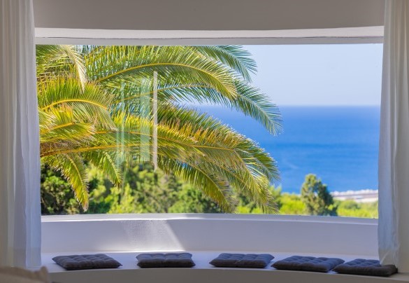 A large living area furnished with a spectacular dining table and sofas placed in front of large windows that frame the boundless panorama - Villa Calypso
