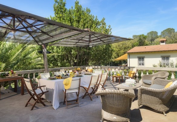 La zona pranzo esterna, piastrellata e delimitata da un colonnato, attrezzata con ombrelloni, tavolo da pranzo e un comodo salottino – Villa Gaius