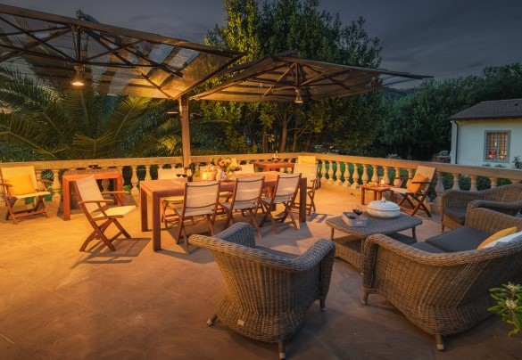 La zona pranzo esterna, piastrellata e delimitata da un colonnato, attrezzata con ombrelloni, tavolo da pranzo e un comodo salottino – Villa Gaius