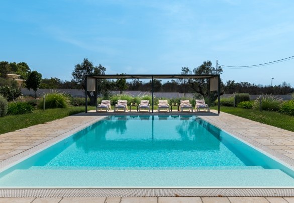 I lettini sono disposti sul lato corto della piscina, sotto uno spazio ombreggiato da una ampia tettoia in legno - Villa I Chiani