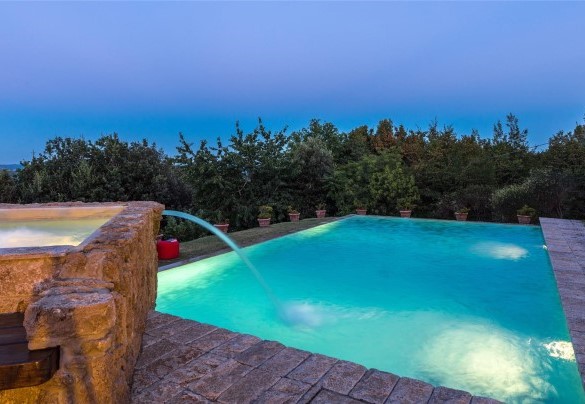 La vasca rettangolare e a sfioro su due lati, rivestita e bordata da pietra di travertino e dotata di gradini di accesso - Villa Il Cedro