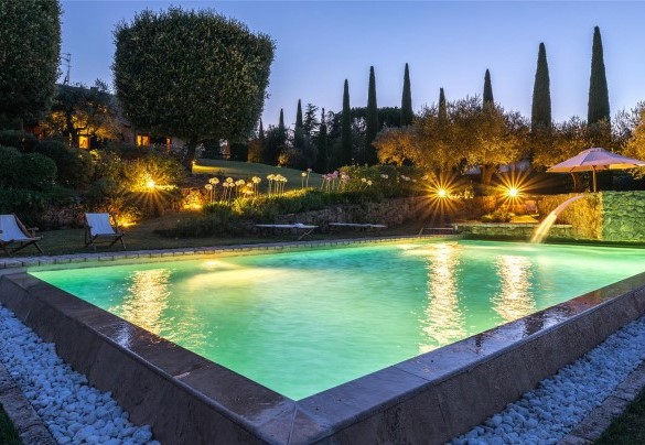 La vasca rettangolare e a sfioro su due lati, rivestita e bordata da pietra di travertino e dotata di gradini di accesso - Villa Il Cedro