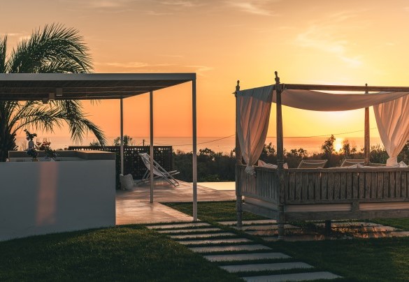 Sul prato regna un prezioso day bed in stile indonesiano con tende parasole, su cui sognare con la magnifica vista del tramonto sul mare – Villa la Pupazza