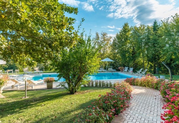 La piscina si raggiunge attraversando il giardino e percorrendo un viottolo lastricato bordato di cespugli fioriti – Villa Leonardo