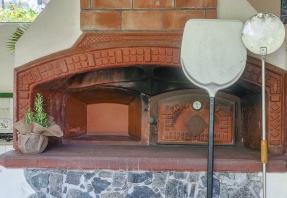 Il forno a legna è accanto alla cucina esterna e, insieme al barbecue in muratura, sono integrati nel grande portico - Villa Liberty Albisola