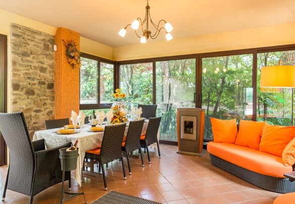 Veranda, completamente rivestita di porte a vetri, allestita con divani e tavolo per mangiare al piano terra – Villa Monica