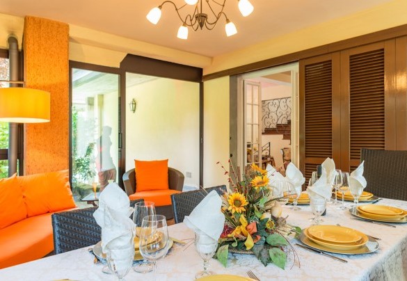 Veranda, completamente rivestita di porte a vetri, allestita con divani e tavolo per mangiare al piano terra – Villa Monica