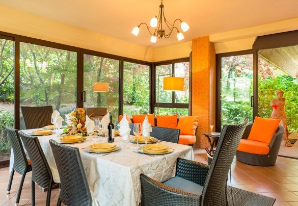 Veranda, completamente rivestita di porte a vetri, allestita con divani e tavolo per mangiare al piano terra – Villa Monica