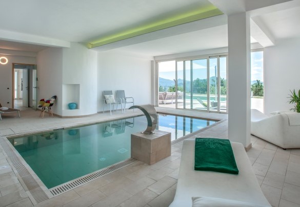 Indoor pool with a water cascade, lounge chairs for relaxation, and a large glass window overlooking the view - Dimora Montefalcone