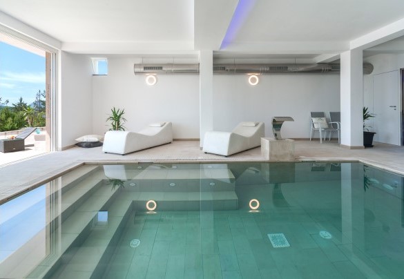 Indoor pool with relaxation seating, soft lighting, and large glass doors overlooking the outside - Dimora Montefalcone