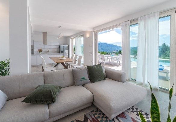 Spacious living room with a sofa, large glass windows brightening the space, and a view of the pool - Dimora Montefalcone