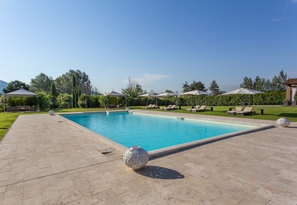 La piscina adiagata su un solarium in travertino e prato - Villa Ginevra