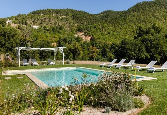 Lungo il perimetro della vasca si sviluppa l’area solarium, a prato, arredata con lettini – Villa Poderina