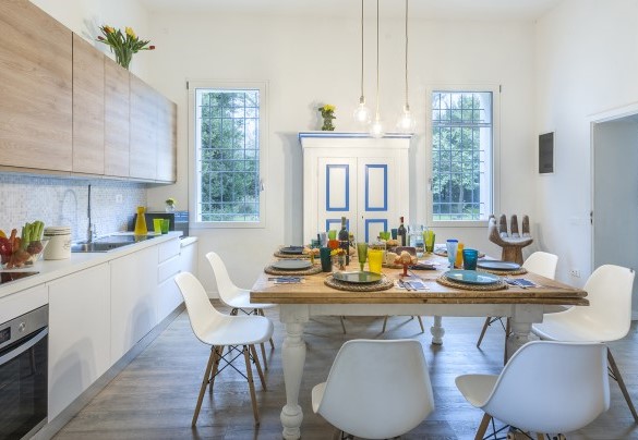 La moderna cucina dove il protagonista indiscusso è il tavolo in legno quadrato posizionato al centro della stanza che favorisce la convivialità e la conversazione – Villa Rustica