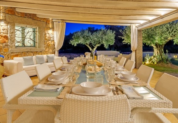 Living esterno impreziosito da travi in legno bianco con elegante tavola in cui trascorrere piacevoli serate estive – Villa Typha