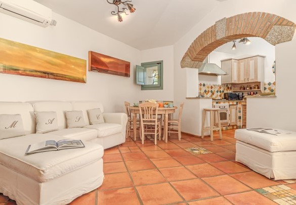Luminoso open space con vetrate che si affacciano sulla veranda e sul giardino in cui troviamo la zona living con divano, tavolo rotondo e la cucina accessoriata – Villa Typha