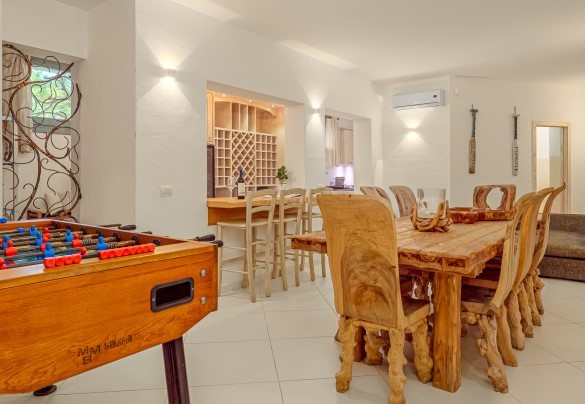 Zona living del piano seminterrato con tavolo in legno, divani e cucina accessoriata – Villa Typha